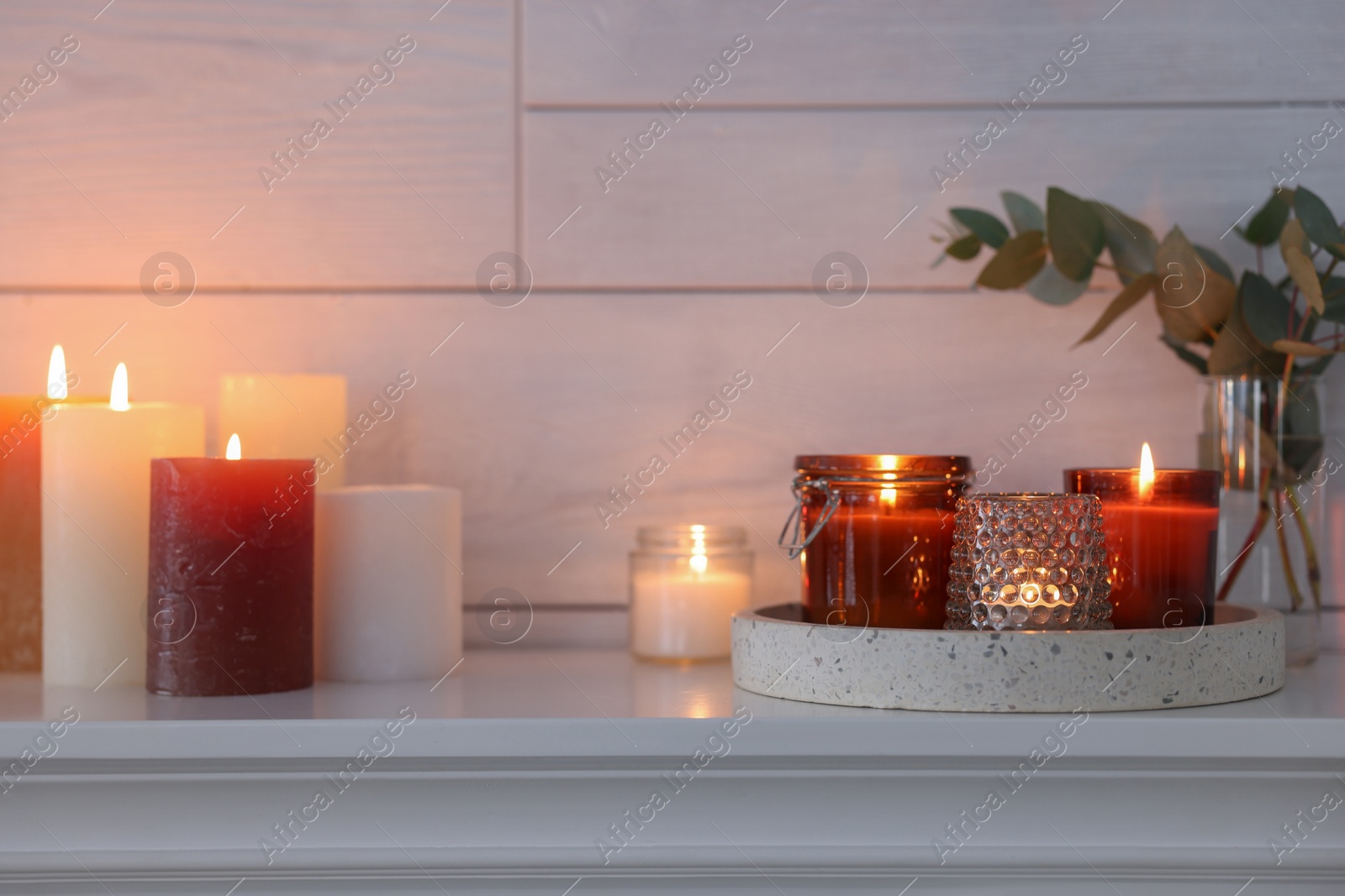 Photo of Burning candles on mantel near white wall indoors