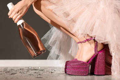 Stylish party. Woman wearing pink high heeled shoes with platform and square toes holding bottle of wine indoors, closeup