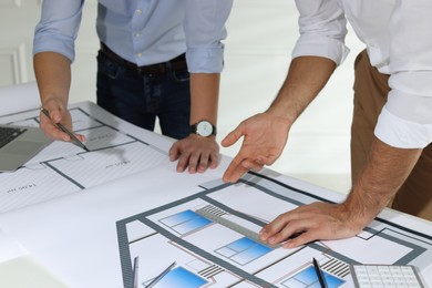 Photo of Architects working with construction drawings at table in office, closeup