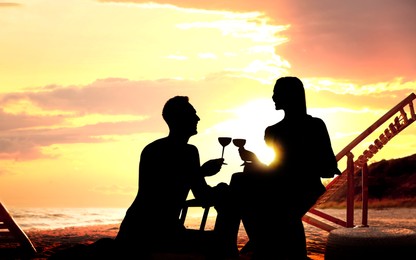 Image of Silhouette of lovely couple drinking wine together on beach at sunset