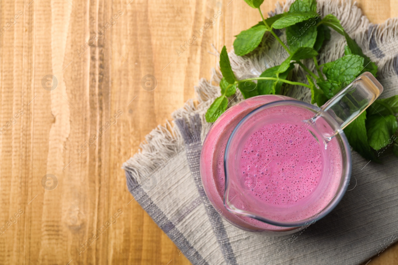 Photo of Glass jug of blackberry smoothie and mint on wooden table, flat lay. Space for text