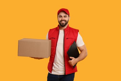 Photo of Happy young courier with parcel and clipboard on orange background