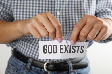 Atheism as religious position. Woman ripping paper with text God Exists on white background, closeup