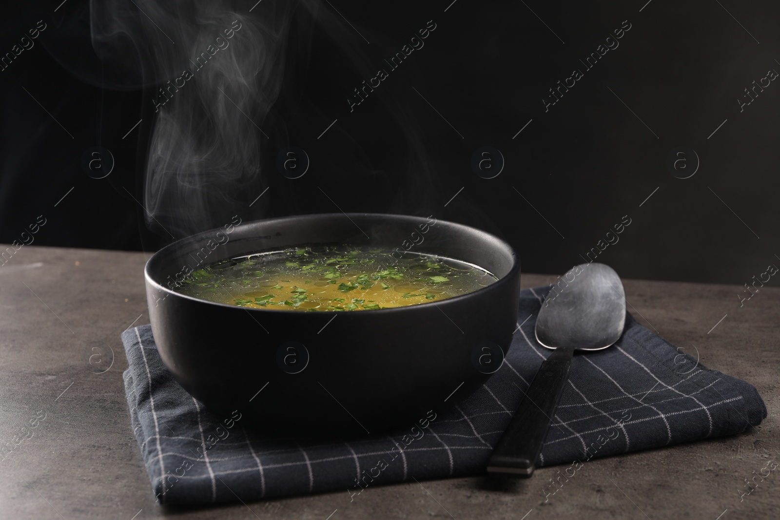 Photo of Delicious soup with parsley and spoon on grey table