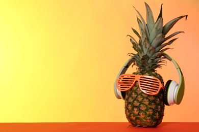 Photo of Funny pineapple with headphones and party glasses on color background, space for text