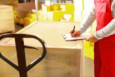 Worker with clipboard near wrapped pallets in warehouse, closeup. Logistics concept