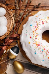 Photo of Delicious Easter cake decorated with sprinkles near painted eggs and willow branches on wooden table, flat lay