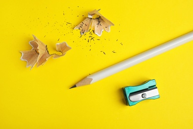 Photo of Pencil, sharpener and shavings on yellow background, flat lay