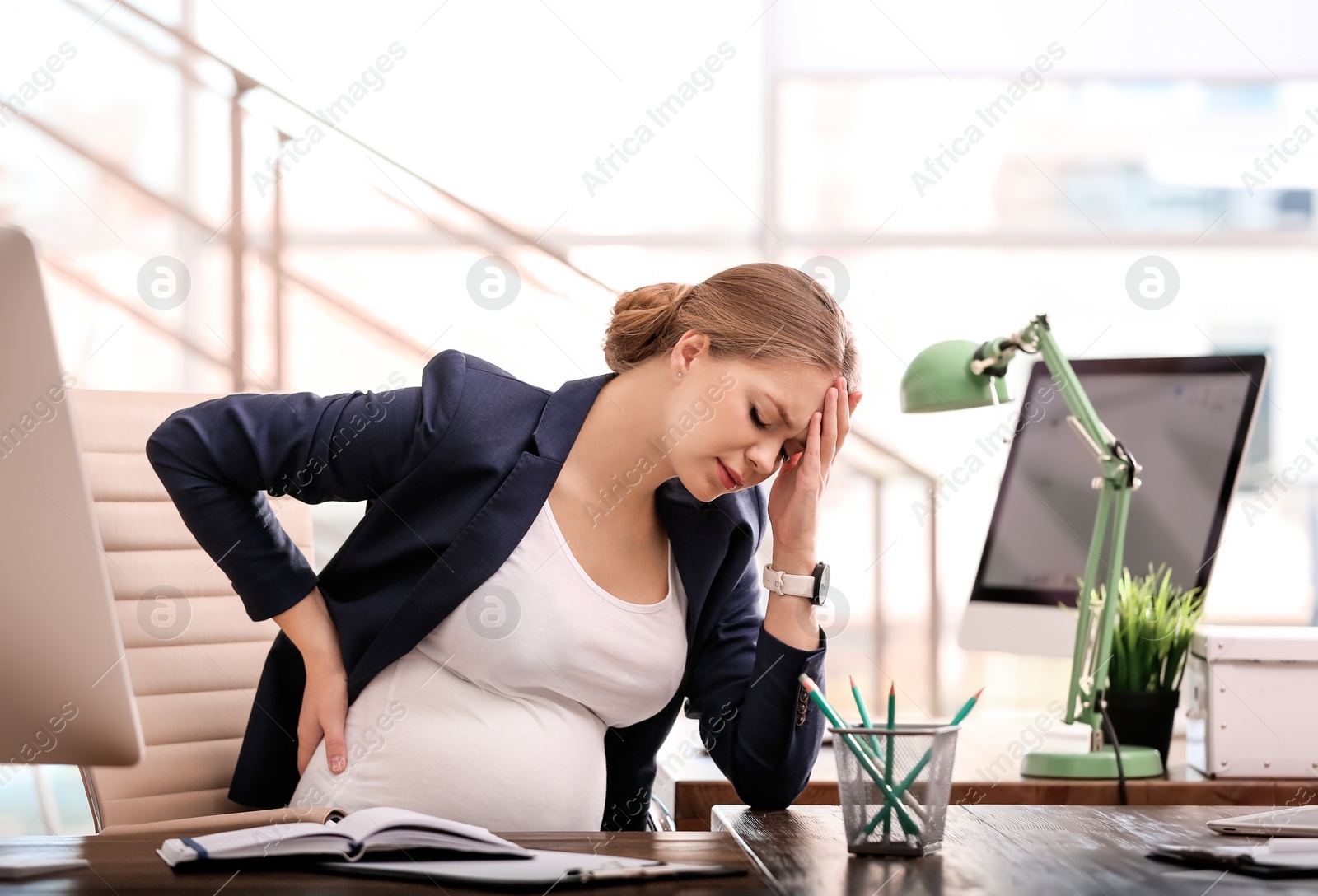Photo of Young pregnant woman suffering from pain while working in office