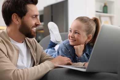 Happy man and his daughter with laptop on sofa at home