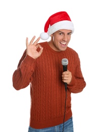 Emotional man in Santa Claus hat singing with microphone on white background. Christmas music