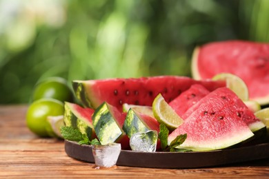 Photo of Slices of delicious ripe watermelon, ice cubes and cut lime on wooden table outdoors, space for text