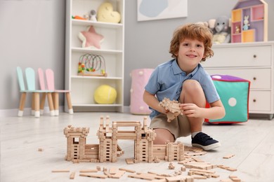 Photo of Little boy playing with wooden construction set on floor in room, space for text. Child's toy