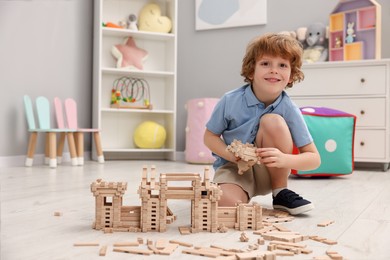 Little boy playing with wooden construction set on floor in room, space for text. Child's toy