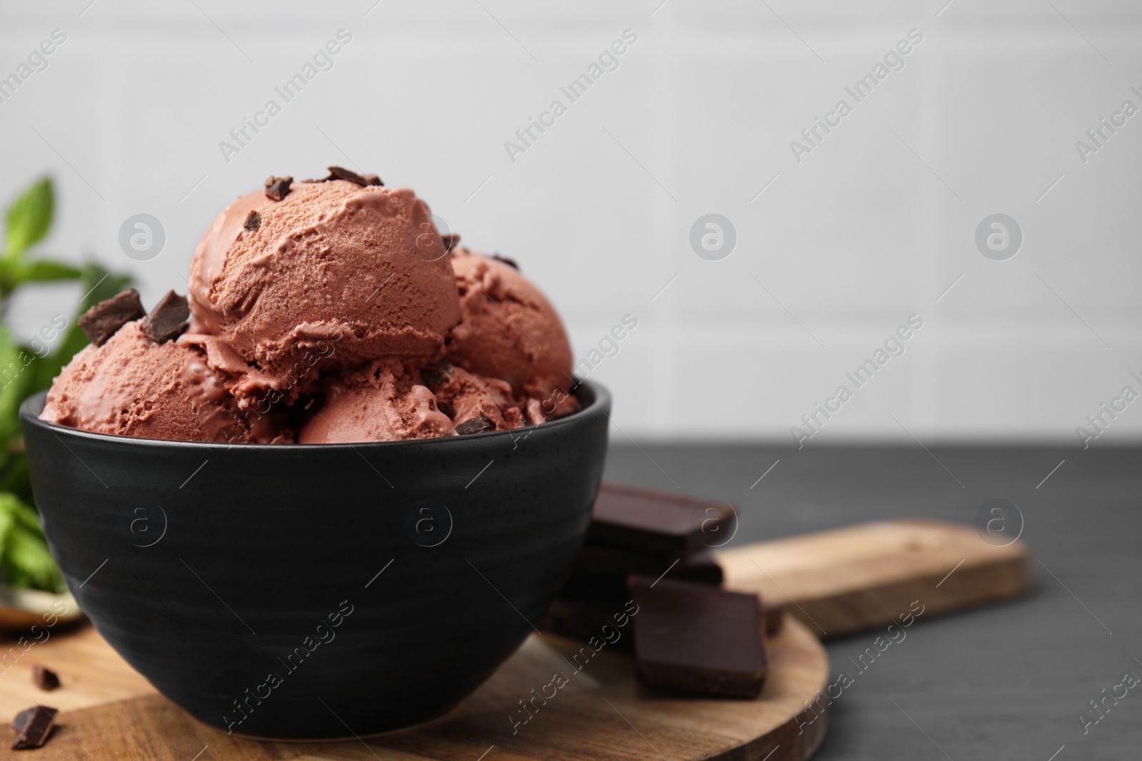 Photo of Bowl with tasty chocolate ice cream on grey wooden table, closeup. Space for text