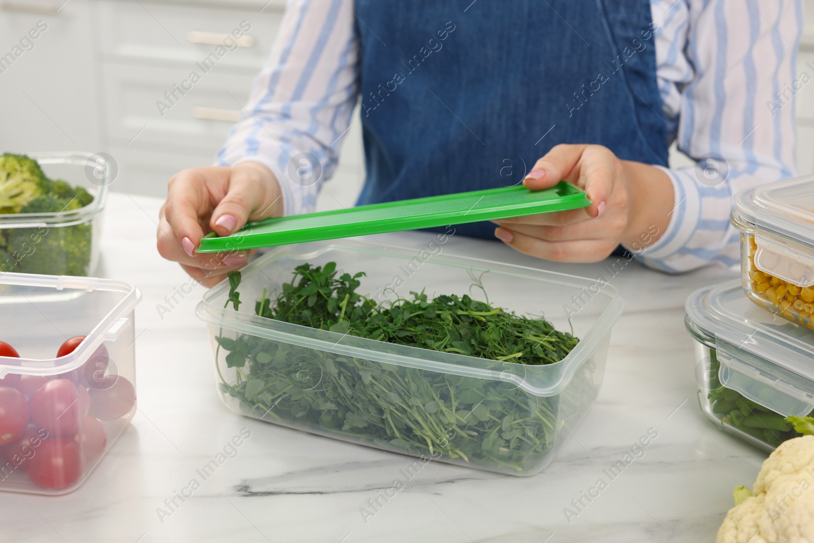 Photo of Woman sealing glass container with greens at white marble table in kitchen, closeup