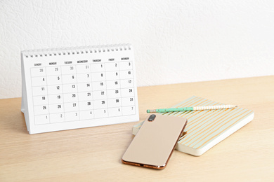 Paper calendar and smartphone on wooden table near white wall