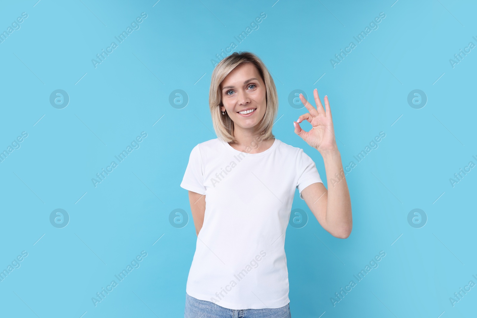 Photo of Happy woman showing ok gesture on light blue background