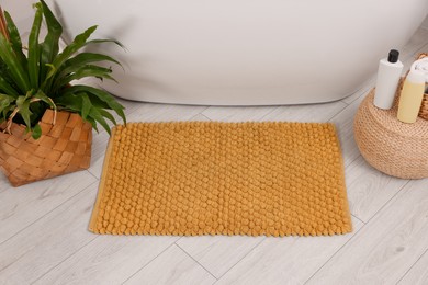 Photo of Soft bath mat, green plant and cosmetic products in bathroom