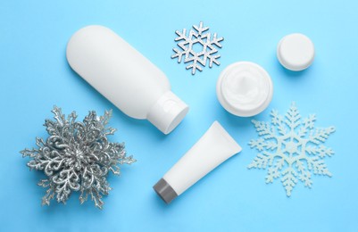 Photo of Flat lay composition with cosmetic products and snowflakes on light blue background. Winter skin care