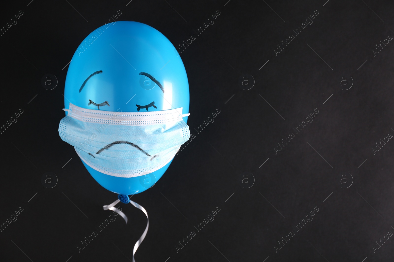 Photo of Air balloon in medical mask with drawn sad face on black background. Space for text