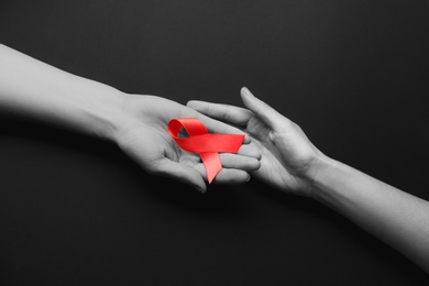 Image of World AIDS disease day. Women holding red awareness ribbon on black background, top view
