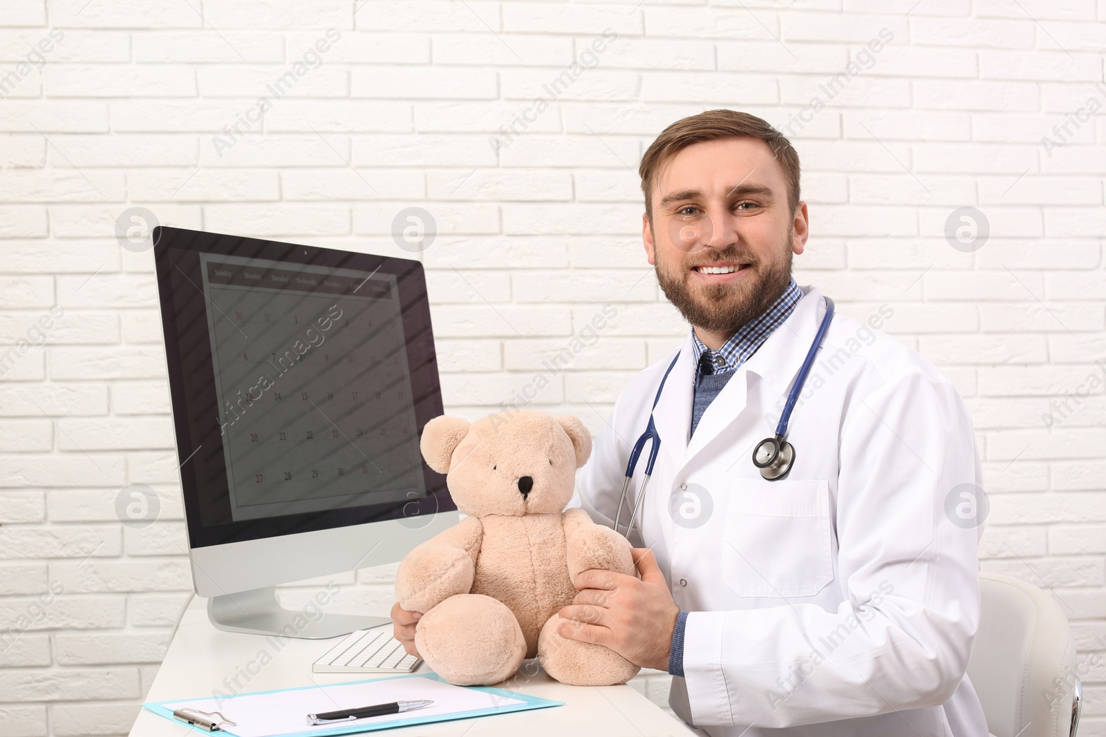 Photo of Pediatrician with teddy bear at table in clinic