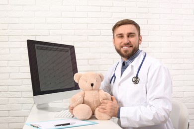 Pediatrician with teddy bear at table in clinic