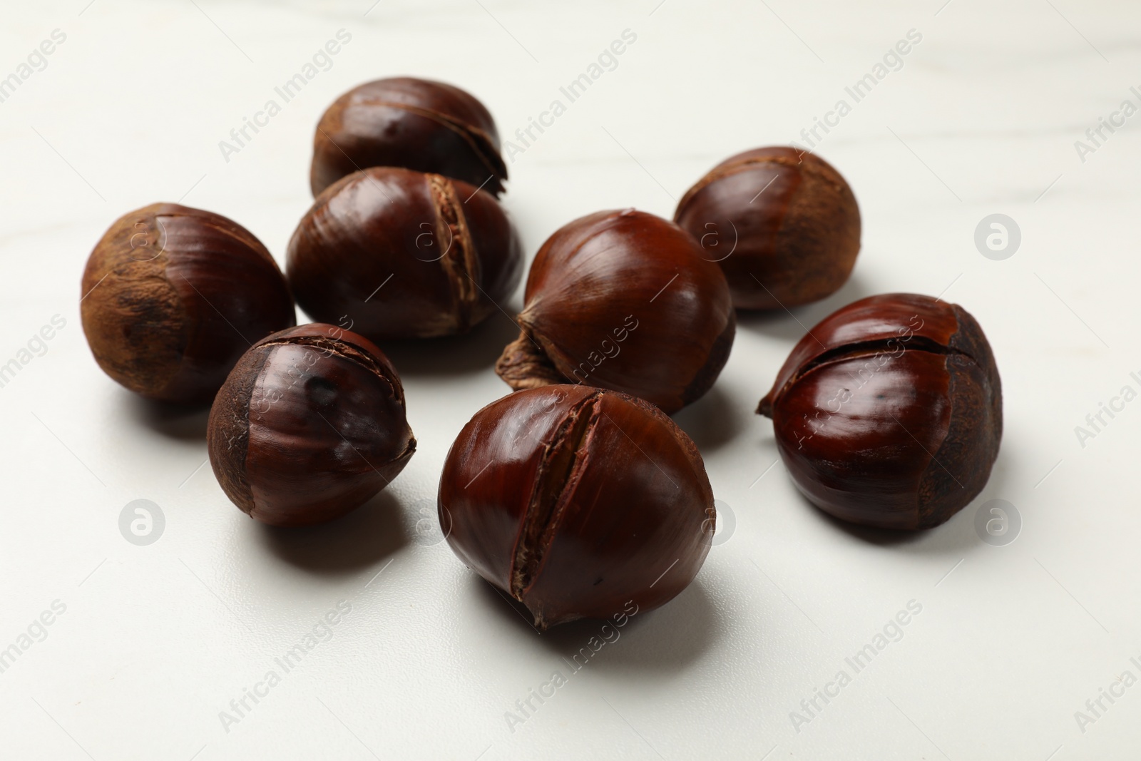 Photo of Roasted edible sweet chestnuts on white table, closeup