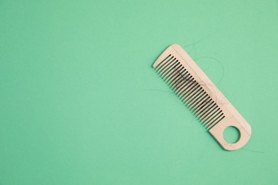 Photo of Wooden comb with lost hair on green background, top view. Space for text