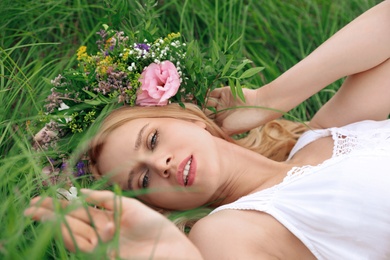 Photo of Young woman wearing wreath made of beautiful flowers on green grass