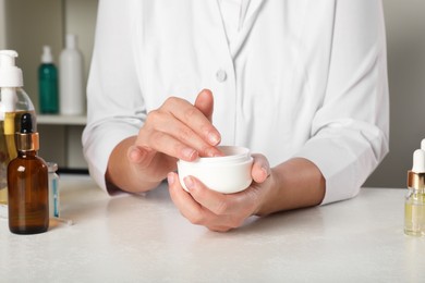 Photo of Dermatologist testing cosmetic product at white table indoors, closeup