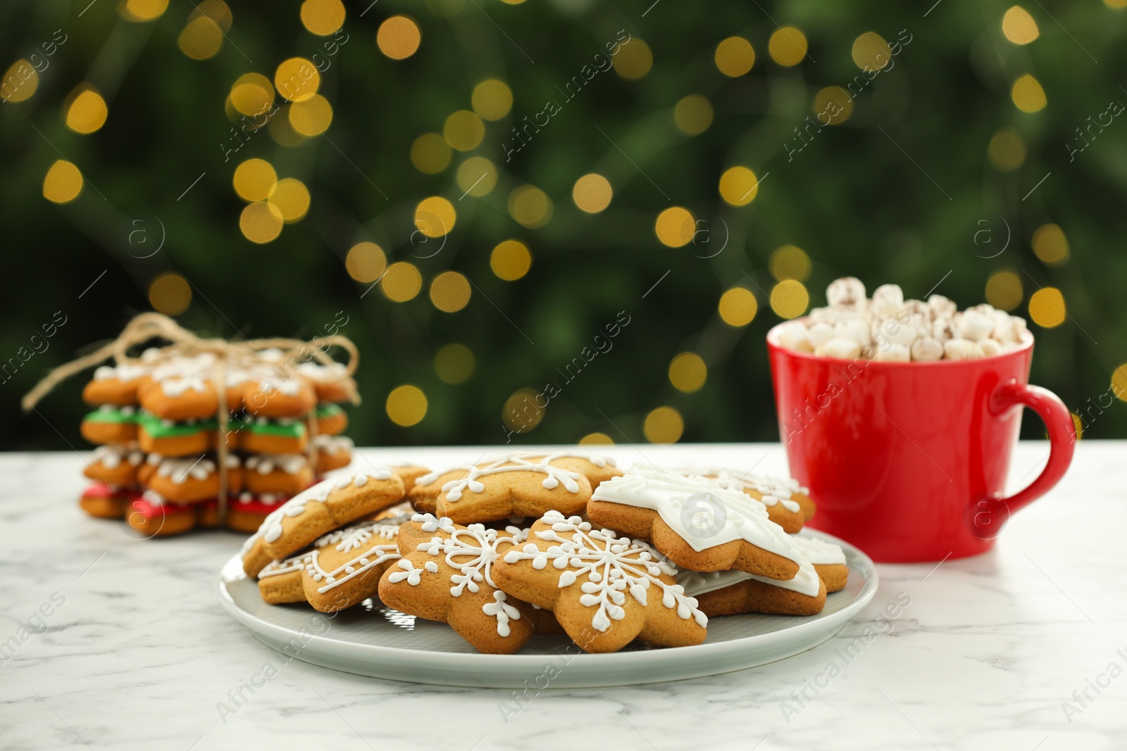 Photo of Decorated cookies and hot drink on white marble table against blurred Christmas lights