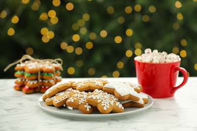 Decorated cookies and hot drink on white marble table against blurred Christmas lights