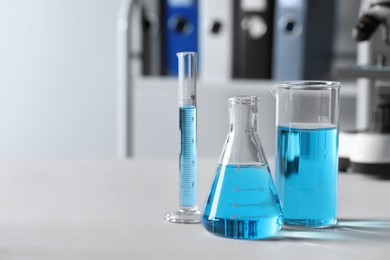 Photo of Different laboratory glassware with light blue liquid on table. Space for text