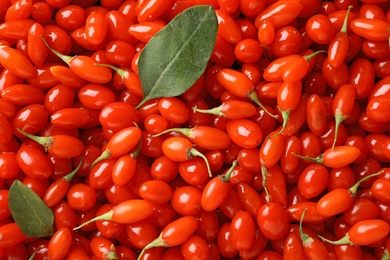 Photo of Fresh ripe goji berries with leaves as background, top view