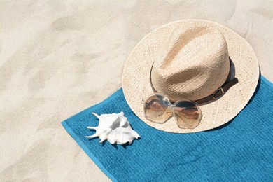 Photo of Soft blue towel, sunglasses, straw hat and seashell on sandy beach