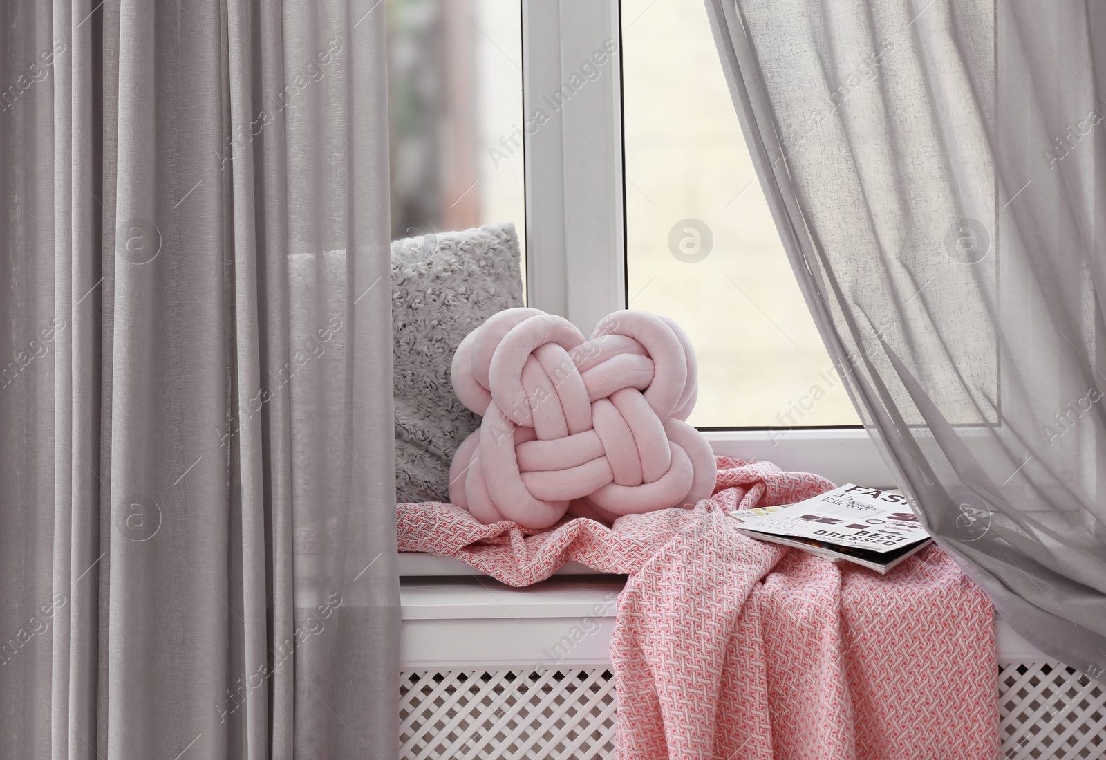 Photo of Cozy place with pillows and plaid on windowsill in room interior. Unusual cushion design