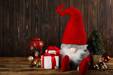 Photo of Cute Christmas gnome, gift boxes and festive decor on wooden table. Space for text