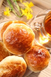 Freshly baked soda water scones, cup of tea and daffodils on wooden table, flat lay