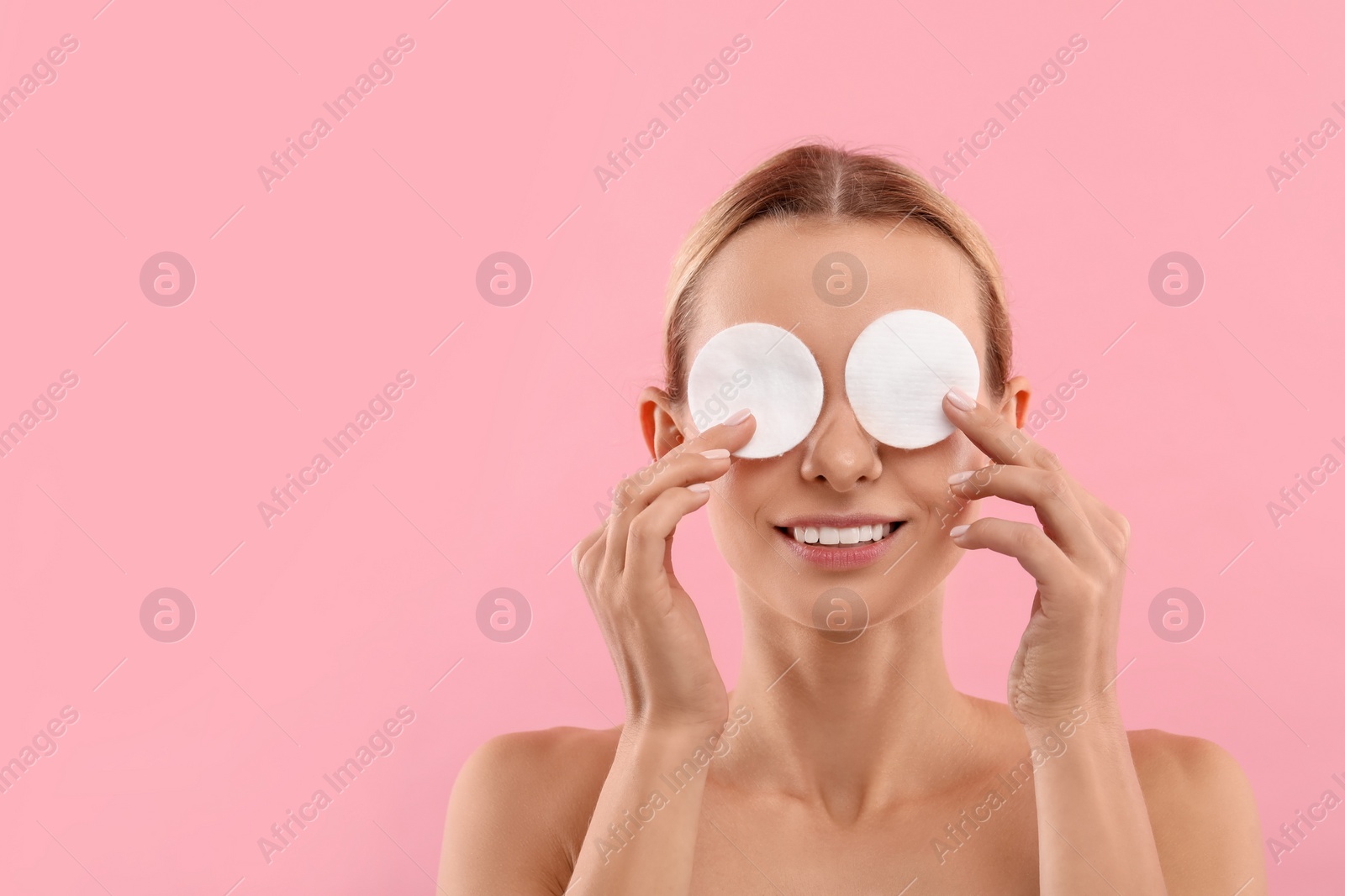 Photo of Smiling woman removing makeup with cotton pads on pink background. Space for text