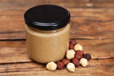 Photo of Tasty nut paste in jar and hazelnuts on wooden table, closeup