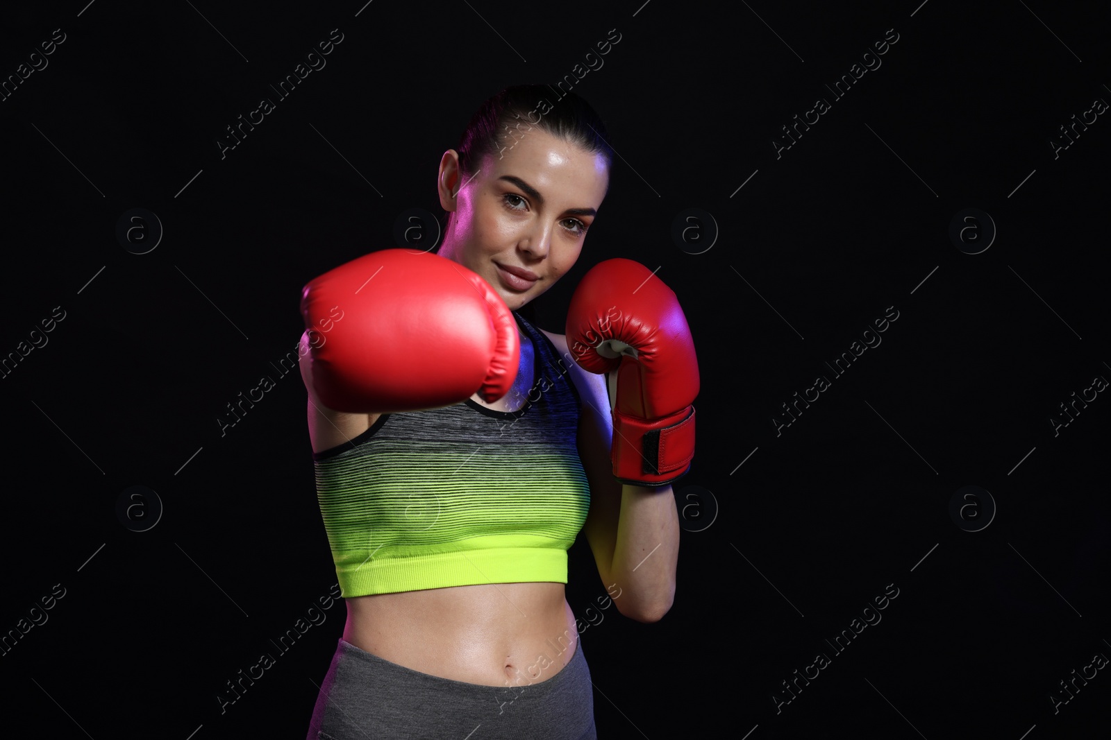 Photo of Portrait of beautiful woman wearing boxing gloves in color lights on black background