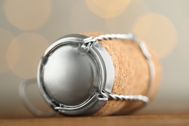 Photo of Sparkling wine cork with muselet cap on table against blurred festive lights, closeup