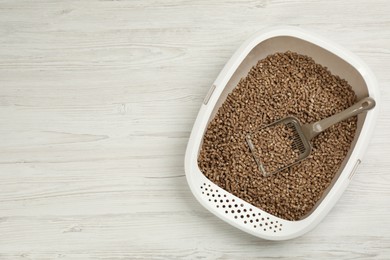 Photo of Cat litter tray with filler and scoop on white wooden floor, top view. Space for text