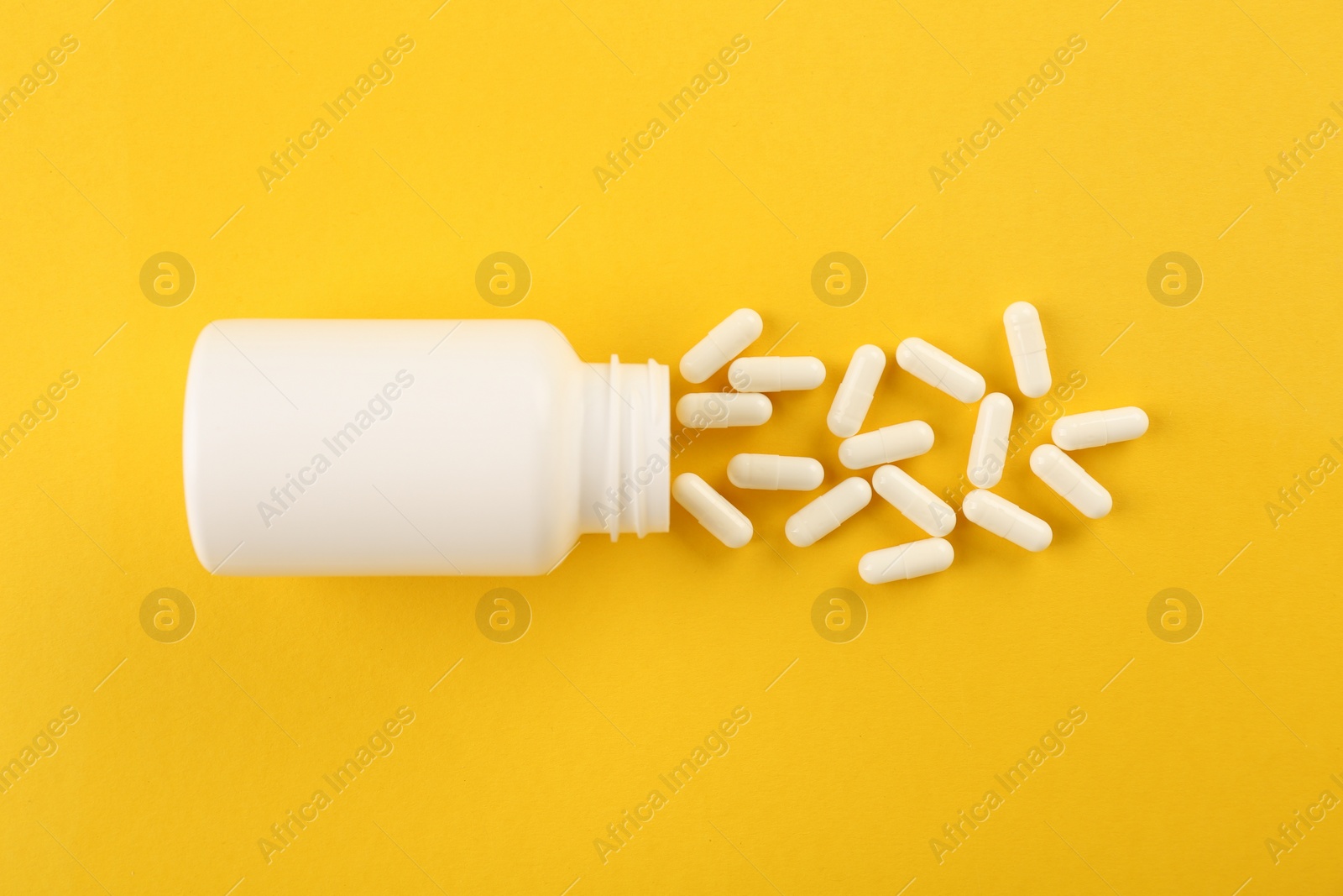 Photo of Bottle and vitamin capsules on yellow background, top view