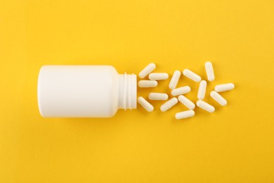 Bottle and vitamin capsules on yellow background, top view