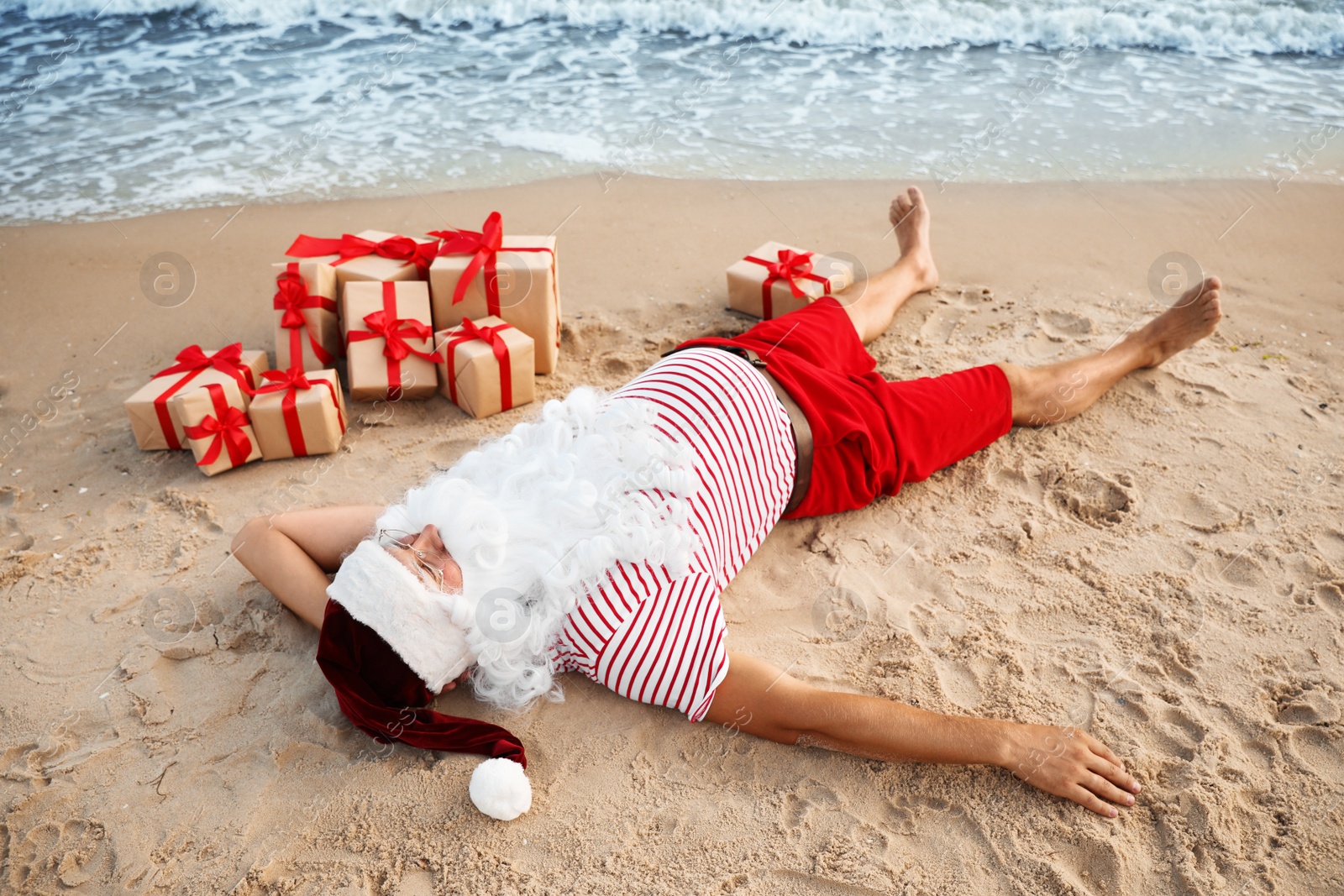 Photo of Santa Claus with presents relaxing on beach. Christmas vacation