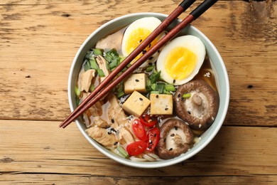 Photo of Bowl of delicious ramen and chopsticks on wooden table, top view. Noodle soup