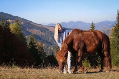 Young woman petting beautiful horse in mountains on sunny day